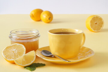 a cup of tea, a jar of honey and lemons scattered on the table - everything is on a table with a yellow tablecloth.