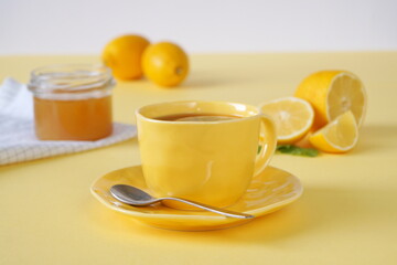 Fototapeta na wymiar tea break - a cup of tea, a jar of honey on a napkin and lemons. The yellow background evokes bright sunny emotions.