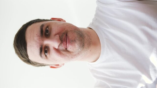 Young man in white t-shirt saying hello during a video call on phone. Vertical video.