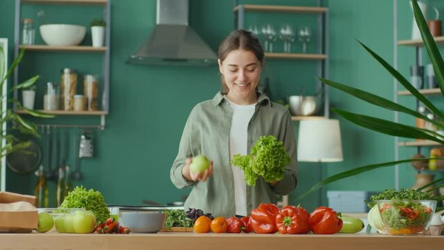 Happy Young Woman Enjoying The Process of Cooking, Having Fun Playing With an Apple at the Kitchen Table with Organic Products. Diet, Proper Nutrition, Raw Food Diet. Nutrition and Dietetics.
