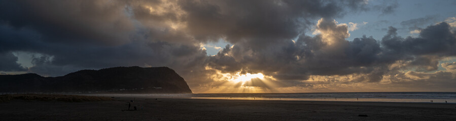 A panorama image of a sun burst at sunset and Tillamook Head headland and the beach at Seaside...