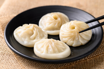 Xiao long bao, small Chinese steamed bun filling with minced pork on black plate eating by use chopsticks