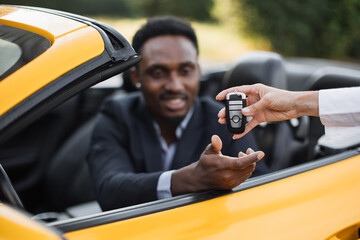 Female auto seller giving keys to male customer form his new sport car. Handsome african man in...