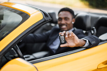 Happy handsome african business man showing car keys in his newly bought auto smiling cheerfully...