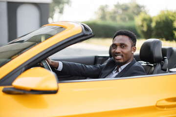 Mature African American business man sitting in the luxury sport vehicle and smiling looking aside....