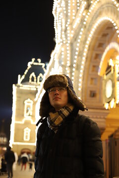 Uzbek guy walking around the Red square in Moscow at night with russian hat.