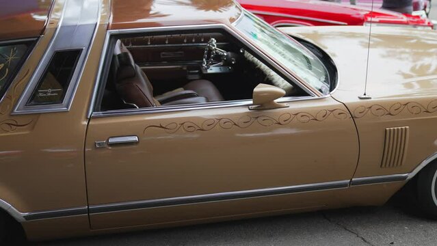 This panning video shows a brown late 1970's Ford Thunderbird lowrider car with a custom paint job.