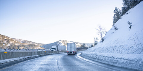 Fototapeta na wymiar Big rigs semi trucks with semi trailers running with cargo toward each other on the winding dangerous slippery winter highway road with snow and ice in the mountain pass in Montana