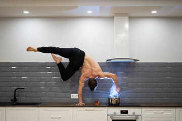 Man keeps balance on one hand and cooks food in the kitchen. Healthy lifestyle, yoga and wellness...