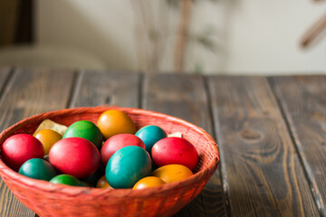 Red wicker basket with colored Easter eggs on a wooden table