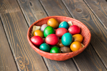 Red wicker basket with colored Easter eggs on a wooden table