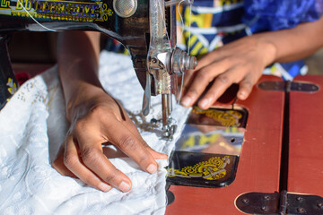 African hands of a tailor or fashion designer making a dress with a sewing machine in a tailoring...