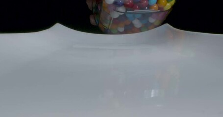 Gumballs spilling onto white platter in reverse shot. Close-up of colorful balls going back up into jar held by a hand, with audio