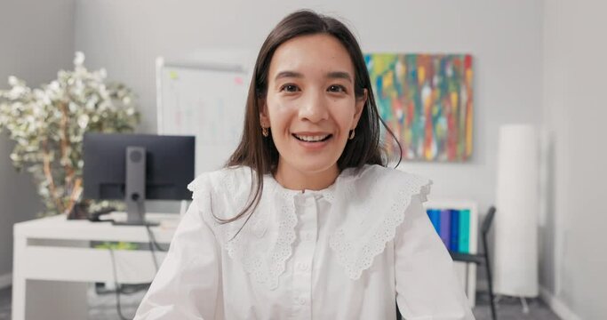 A mature beautiful woman in a white shirt working in an office has a break video chatting with a colleague via computer, waving hand at webcam, listening to her friend's horrible story