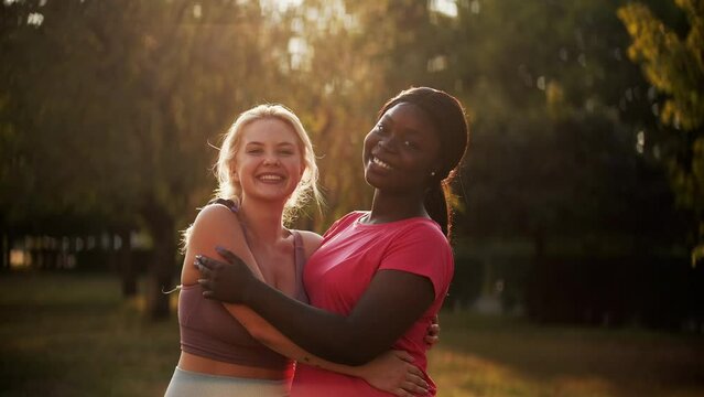Fitness friends. Sport diversity. Outdoor activity. Healthy lifestyle. Happy multiracial women buddies in activewear smiling hugging together at autumn park lens flare.
