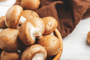 Raw brown champignon mushrooms in wooden olive bowl, old white kitchen table, top view, negative space