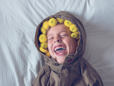 Happy Preteen Boy On Bed With Pom Flowers Under Hood