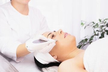 Woman undergoing face cosmetology treatment in a clinic facial procedure, cosmetologist using ultrasonic skin equipment.