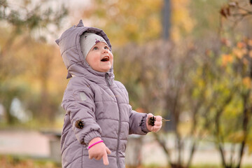 A little girl in a dinosaur jacket is playing with autumn leaves.