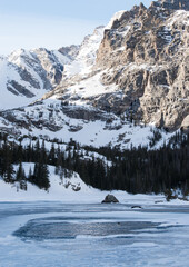 An ice covered alpine lake with steep mountains covered with winter snow in the background at Rocky Mountain National Park Colorado