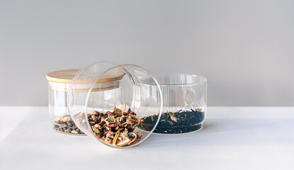 Different types of tea in glass jars on a light background, isolated.
