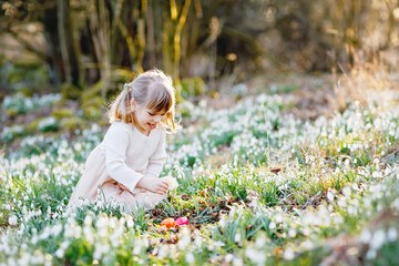Little girl making Easter egg hunt in spring forest on sunny day, outdoors. Cute happy child with...