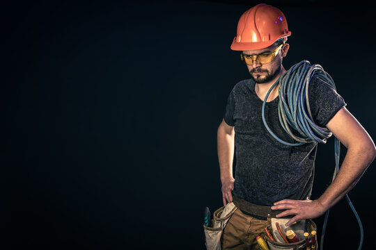 Male electrician with electric cable on a black background, copy space.