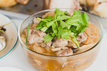 Braised Fish Maw in red gravy and pork ribs with green celery topping in a glass bowl on white table.
