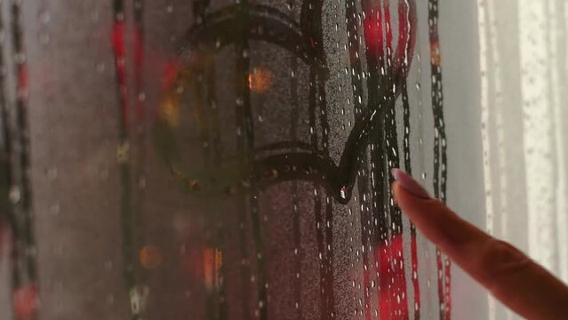 A woman draws a heart with her finger on a fogged window, a close-up of her hand.Christmas,New Year's ,St.Valentines day concept.Slow motion.
