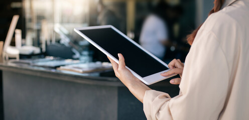 Young asian woman using digital tablet working online and standing in front of the counter in her...