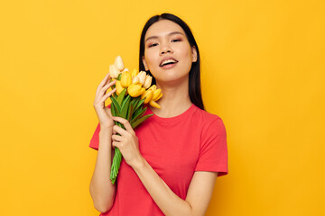cheerful cute asian girl with a bouquet of flowers yellow background