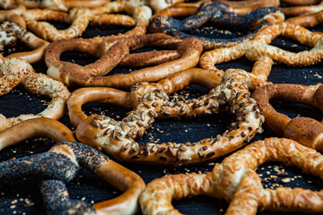 Fresh prepared homemade soft pretzels. Different types of baked bagels with seeds on a black background.