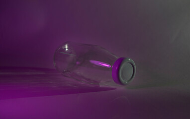 A glass milk bottle with a white lid lies on a dark background. Neon purple light. Blank mock up