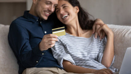 Close up happy couple paying online, focus on gold credit card in man hand, smiling girlfriend and boyfriend shopping in internet, making secure payment, checking balance, banking service