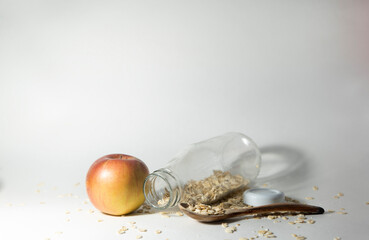 A glass bottle on a white background inside oatmeal. next to it is a red and yellow apple and a wooden spoon. Blank make up. The concept of healthy eating on the way