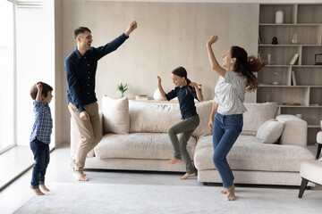 Happy family with two kids dancing in living room together, moving to music, laughing mother and...
