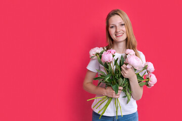 Beautiful young lady with spring flowers celebrating women's day, advertising her product on bright pink studio background, mockup. Beautiful blonde woman holding bouquet of pink peonies, copy space.