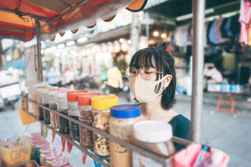 Happy young adult asian foodie woman order vendor asia dessert. Wear face mask for virus. People traveling with new normal lifestyle at outdoor street night food market.