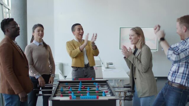 Young handsome casual multiethnic business people playing table football and relaxing at office