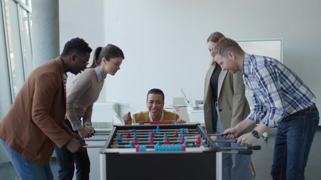 Young handsome casual multiethnic business people playing table football and relaxing at office
