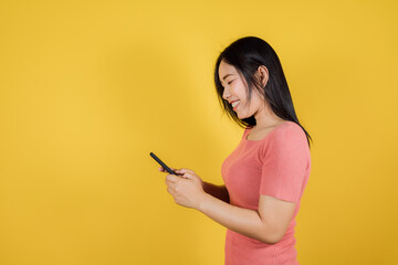Portrait of smiling asian teenager is using mobile phone or smartphone on yellow background. copy space