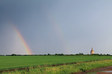 Rainbow in field in front of church