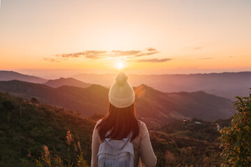 Happy young woman traveler relaxing and looking at the beautiful sunset on the top of mountain