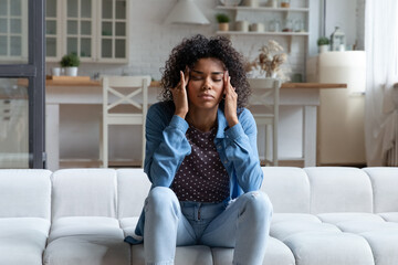 Unhappy stressed young African American woman massaging temples, feeling stressed of noisy disturbing neighbors, suffering from headache, feeling exhausted hearing sound of repairment works at home.