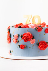 Birthday cake with blue cream cheese frosting decorated with red flowers on the white background. Happy 70 years anniversary