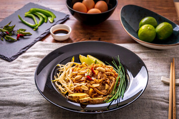 Pad thai close up with lime, chilli and peanuts in a black dish