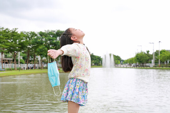 Portrait Of Asian Little Girl Kid Relax Breathing Deep Fresh Air Relieving Taking Off Mask Due Covid-19 On The Nature Garden.