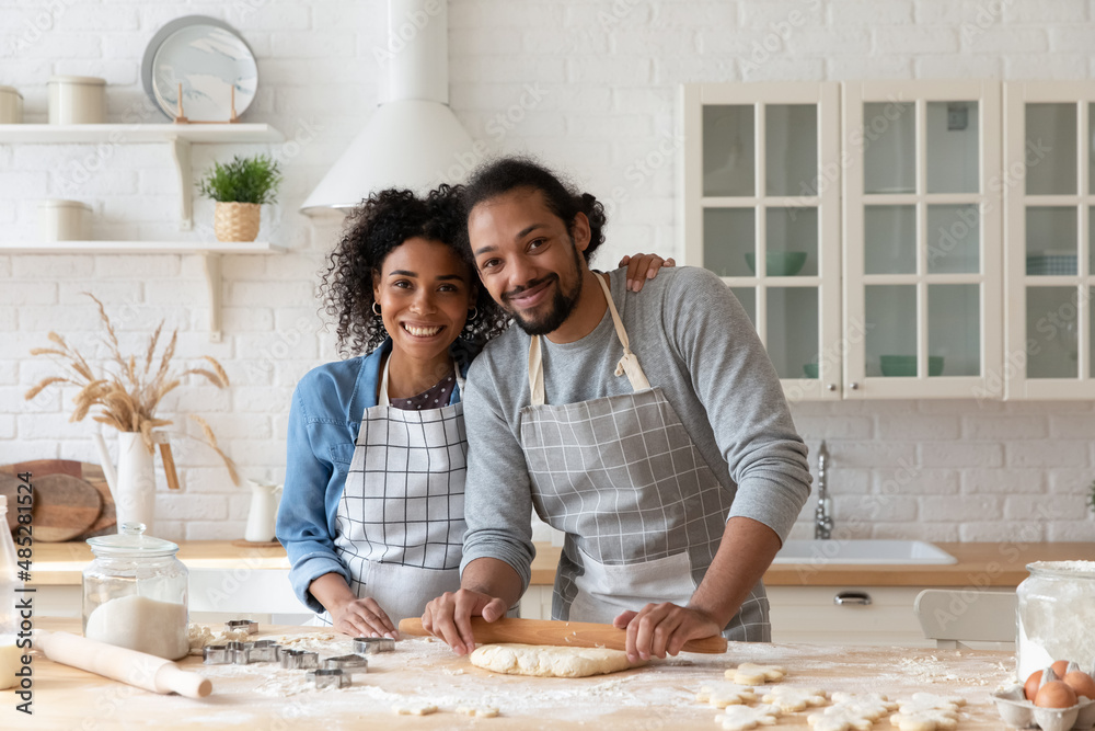 Wall mural portrait of happy loving bonding affectionate young african american family couple in aprons rolling