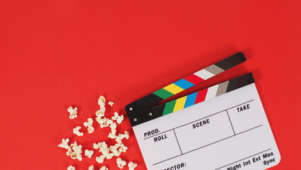 Clapper board or movie slate and popcorn on a red background.