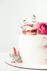 Beautiful birthday cake with pink cream cheese frosting decorated with macaroons and roses. Happy Valentine's day. Anniversary cake on the white background